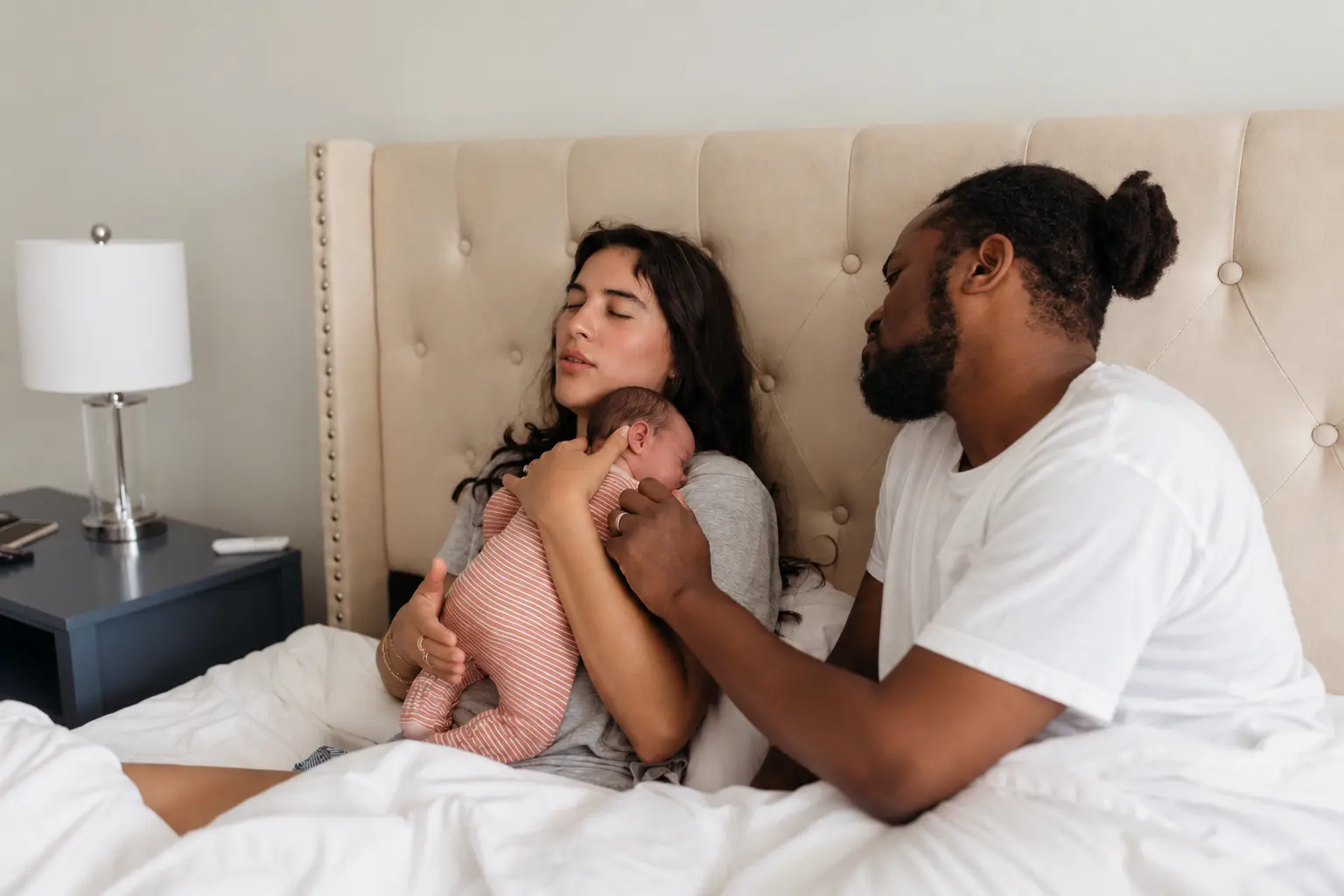 Two parents holding their newborn by a window